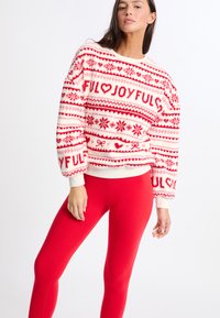 Czerwony i biały sweter z dzianiny z wzorami serc i płatków śniegu, okrągłym dekoltem i ściągaczami na mankietach. Połączony z dopasowanymi czerwonymi legginsami.