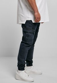 Mörkblå cargo-byxor med elastiska cuffar, flera fickor och en lätt glans. Kombinerat med vita sneakers och en lång vit T-shirt.