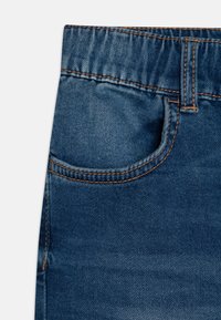 Tissu en denim d'un bleu moyen avec une finition texturée. Comprend une poche arrière et des coutures contrastées visibles le long des coutures.