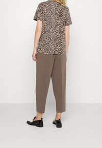 Shortsleeve shirt met luipaardprint gemaakt van zachte stof, gecombineerd met losse beige broek. Zwarte instappers maken de outfit compleet.