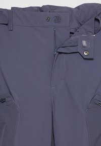 Pantalons d'extérieur bleu marine avec fermeture éclair, bouton et taille ajustable. Comprend des poches latérales avec zips et des coutures renforcées.
