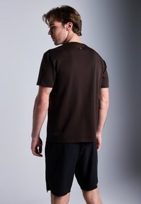 Brun kortermet t-skjorte med rund hals, myk tekstur, kombinert med sorte treningsshorts, som viser en avslappet passform og uformell design.