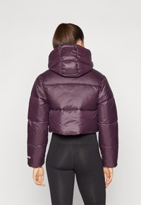 Giacca puffer cropped viola con capuccio grande, caratterizzata da un esterno lucido e un design trapuntato. Polsini elastici e silhouette aderente.