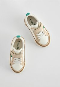 Weiße Sneakers mit beigen Wildlederelementen, grünem Fersenschlaufenelement, elastischen Schnürsenkeln und Klettverschluss. Gummisohle mit weißen Nahtdetails.