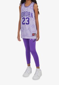 Maglia a rete viola con la scritta "JORDAN 23" in lettere grassetto. Abbinata a leggings viola e scarpe da ginnastica bianche. Dettagli floreali e accenti con logo.