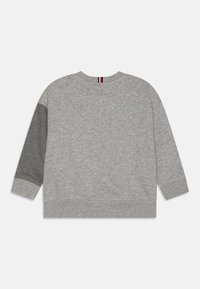 Felpa grigia con maniche lunghe, presenta un pannello grigio più chiaro su una manica e un colletto a coste. Texture sottile su tutta la superficie.
