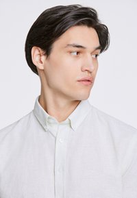 Ljusgrön skjorta med knappar i en strukturerad tygkvalitet, med krage, vita knappar och en semi-strukturerad passform. Minimalistisk design.