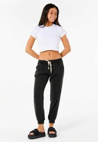 Hvid crop top, sorte joggingbukser med elastisk talje og snor, og sorte platform sandaler; modellen poserer med hænderne på hofterne.