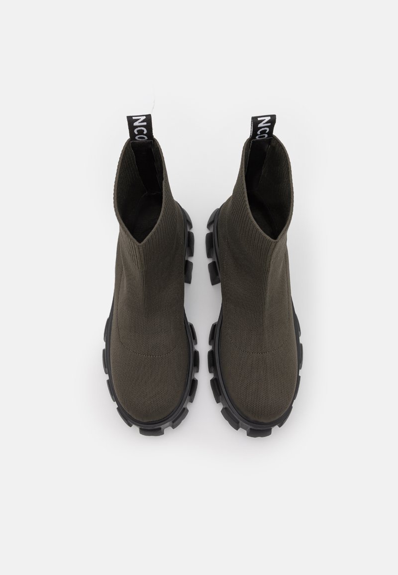 Bottes de cheville vert foncé avec une texture côtelée, dotées d'une languette de traction et d'une semelle en caoutchouc noir épais avec des crampons proéminents pour une meilleure adhérence.