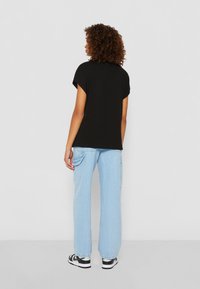 T-shirt noire à manches courtes, associée à un jean léger bleu clair à coupe décontractée et des baskets noires et blanches. Vue de dos sur un fond neutre.