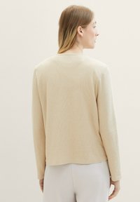 Beige långärmad tröja i texturerad tyg, med rund halsringning och rak passform, med en enfärgad baksida och inga synliga dekorationer.