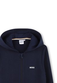 Sweatshirt com fecho éclair na cor azul marinho, apresentando um capuz com cordão, logotipo branco no peito, tecido macio e um forro interior contrastante.