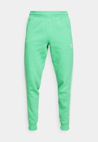 Pantalones de chándal verdes de algodón con cintura elástica, bolsillos laterales y rayas blancas a los lados. Presenta un pequeño logo en el muslo. Textura suave.