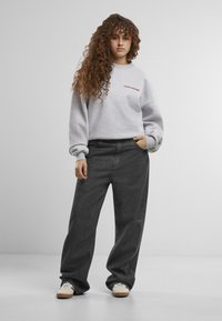 Grå hettegenser med rød brodert tekst, kombinert med løst sittende svarte jeans. Ensfarget design, uformell stil, myk stoff.