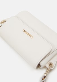 Sac bandoulière en cuir blanc texturé avec quincaillerie dorée. Il dispose d'une fermeture à rabat et d'un logo embossé à l'avant. Mesures non fournies.