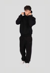 Czarna bluza z kapturem z przednią kieszenią, zestawiona z czarnymi spodniami dresowymi z subtelnym logo. Całość dopełniają białe trampki.