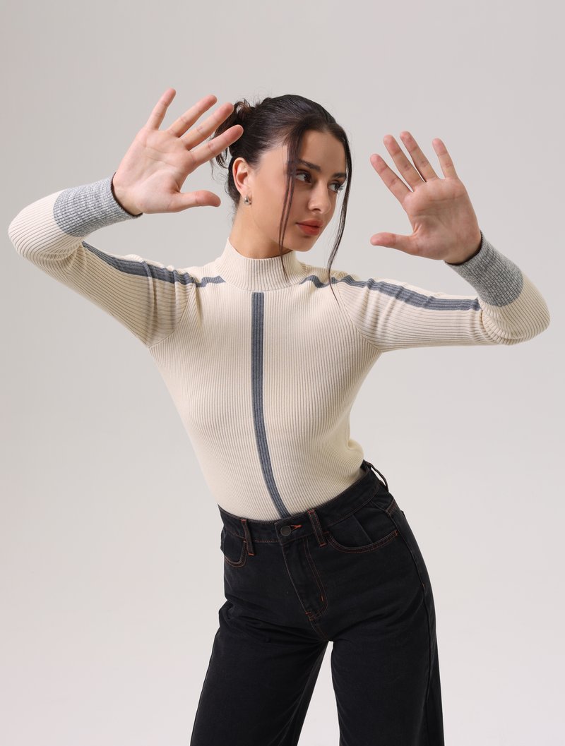 Rippstrick-Turtleneck-Oberteil in Creme mit grauen Akzenten, mit einer figurbetonten Silhouette. Kombiniert mit schwarzen High-Waist-Jeans.