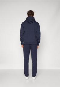 Himmelblauer Baumwollhoodie mit hohem Kragen und verstellbaren Kordeln, kombiniert mit passenden Hosen. Geschmeidige Textur, lockere Passform.
