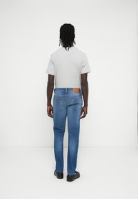 Γκρι κοντομάνικη μπλούζα συνδυασμένη με μπλε τζιν τζιν, διαθέτει δερμάτινο έμπλαστρο στη ζώνη πίσω από τη μέση. Μαύρα παπούτσια ολοκληρώνουν το σύνολο.