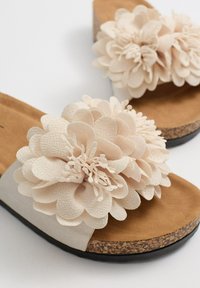 Chanclas de color beige con adornos florales, parte superior de tejido suave, plantilla de corcho y suela plana de goma negra.