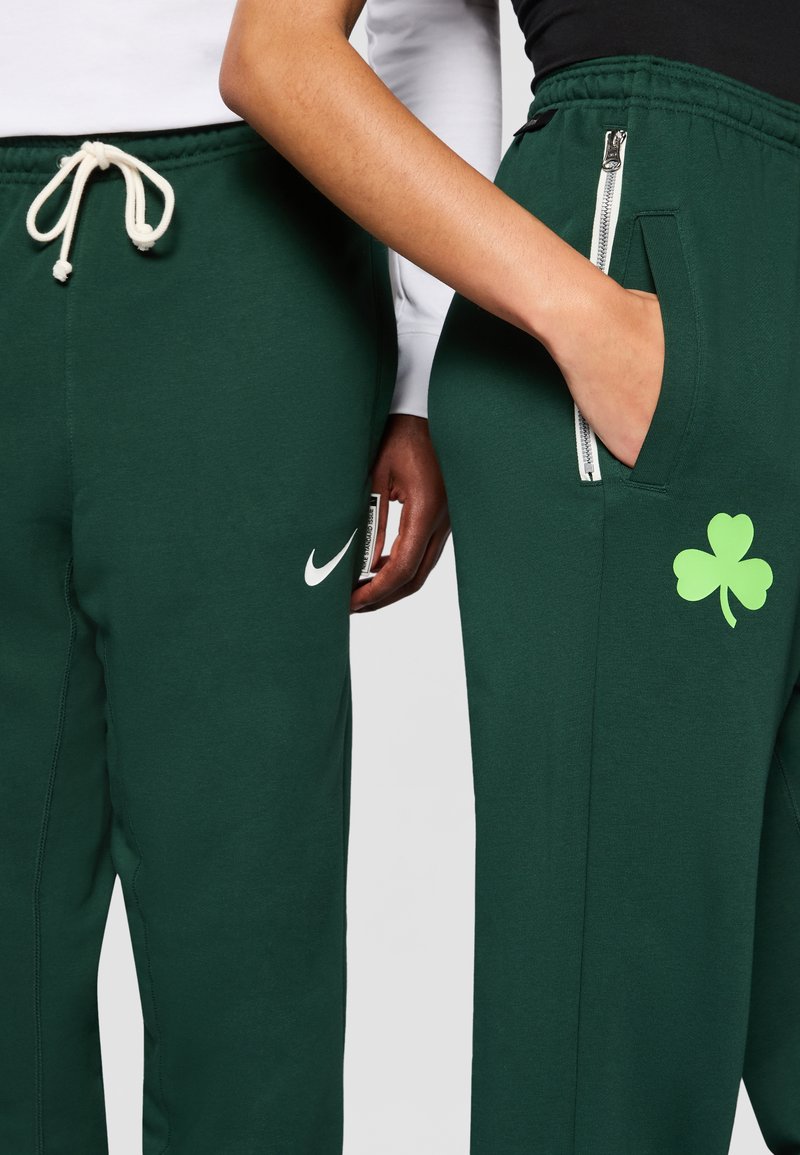 Pantaloni del suor verdi in morbido tessuto, dotati di logo Nike, tasca laterale con zip e un design di trifoglio verde sulla coscia.