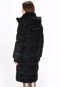 Czarna pikowana kurtka puchowa z teksturowanym wykończeniem, kapturem i długimi rękawami. Posiada zamek błyskawiczny oraz elastyczne mankiety, o długości do połowy uda.