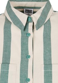 Camicia con colletto a righe verticali verdi e beige, bottoni turchesi, due tasche frontali e un'etichetta "Urban Classics" all'interno del colletto.