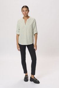 Ljusgrön randig blus med v-ringning och uppvikta ärmar, kombinerad med svarta slim-fit byxor och svarta loafers med ett guldaccent.