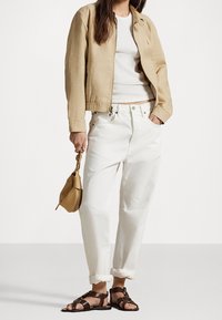 Hnědá bomber bunda, bílý top na ramínka, bílé džínové kalhoty s krátkým rukávem, hnědé sandály a malá zlatá kabelka s pleteným popruhem.