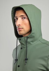 Green waterproof jacket with a hood, featuring black drawstrings and buttons. Smooth texture, sleek design, and minimal detailing.
