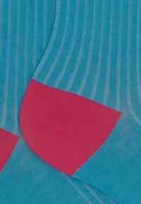 Calzini turchesi con texture a coste verticali e talloni rosa brillante. Il materiale sembra morbido ed elastico.