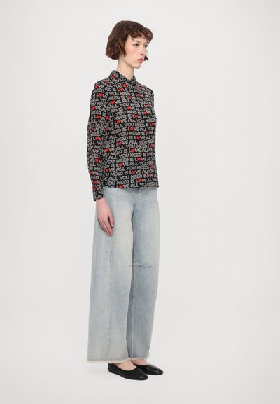 Black button-up shirt featuring red and white text patterns, paired with light blue wide-leg denim jeans and black slip-on shoes.