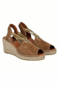 Sandalias de cuña de ante marrón con punta abierta, suela de yute trenzado y lazos entrecruzados sujetos por un detalle de metal en tono plateado.