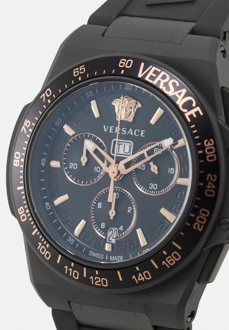 Svart klocka med roseguld-accenter, rund urtavla, tre underdials och Versace-logotyp. Har en gummiband och texturerad bezel.