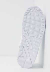 Weißer Gummisneaker-Sohlen mit strukturierten Griffmustern und prominenter Nike-Markierung. Merkmale sind kantige Formen und abgerundete Kanten.