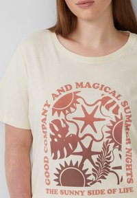 Crème-kleurige katoenen t-shirt met een rood grafisch ontwerp met zon- en plantenmotieven, ronde halslijn en korte mouwen.