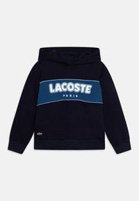 Sweat-shirt à capuche bleu marine avec un grand logo blanc "LACOSTE PARIS" sur la poitrine et un petit emblème de crocodile vert sur l'ourlet.
