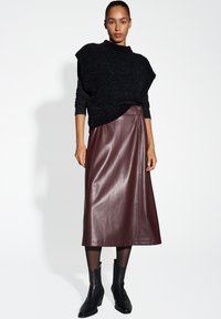 Schwarzer strukturierter Strickpullover mit hohem Kragen, kombiniert mit einem burgunderfarbenen Kunstlederrock und schwarzen Ankle Boots. Glatte, elegante Optik.