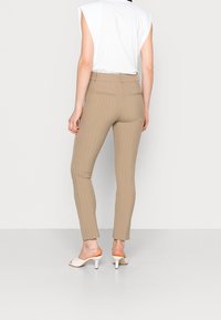 Pantaloni beige sartoriali con righe verticali, design aderente, due tasche posteriori, abbinati a un top bianco morbido e sandali con punta aperta.