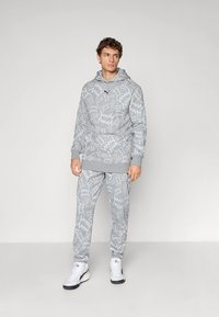 Grauer Hoodie und Jogginganzug. Beinhaltet abstraktes Muster, Kapuze mit Kordelzug, Kängurutasche und gerippte Bündchen. Kombiniert mit weißen Sneakern.