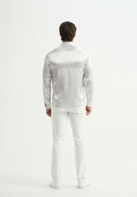 Chemise blanche en satin à manches longues avec ourlet arrondi, poignets à boutons et texture lisse, associée à un pantalon blanc ajusté et des baskets.
