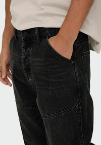 Jeans de mezclilla negra con un corte recto, que cuentan con un diseño de cinco bolsillos, una textura sutil y detalles de costura visibles.