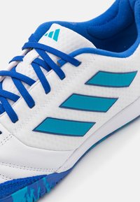 Bílé sportovní boty s modrými akcenty, s texturovaným svrškem, kontrastními tkaničkami a třemi modrými pruhy na boku.