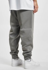 Pantalones jogger grises hechos de tela suave, con un corte relajado, puños elásticos en los tobillos y combinados con zapatillas blancas.