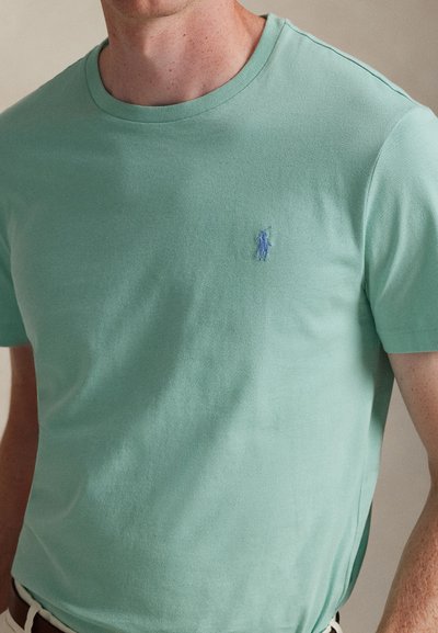 Ανοιχτό πράσινο βαμβακερό μπλουζάκι με στρογγυλή λαιμόκοψη και κοντά μανίκια, με μικρό μπλε κεντημένο λογότυπο στο αριστερό μέρος του στήθους.