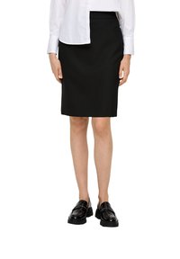 Zwarte kokerrok, knielang, gemaakt van een gladde stof. Gecombineerd met een witte blouse en zwarte gepolijste instappers. Geen patronen of accenten.
