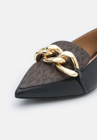 Mocassin pointu noir et marron avec dessus texturé et grand détail de chaîne dorée brillante à l'avant.