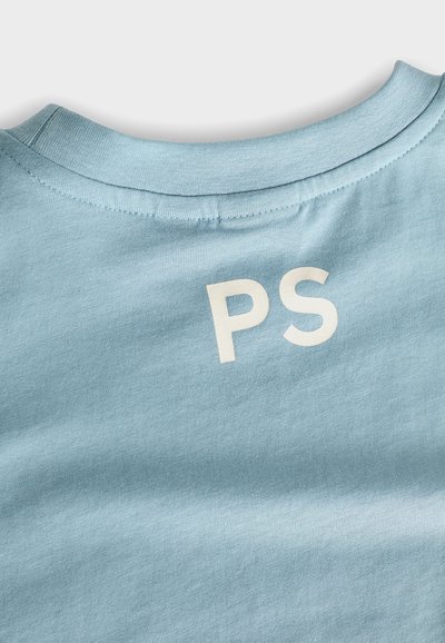 Gaiši zila kokvilnas T-kreklu ar apaļu kaklu un baltu "PS" logotipu uz muguras. Mīksta tekstūra ar gludu apdari.