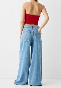 Rotes trägerloses Crop-Top, kombiniert mit weiten blauen Jeans. Die Jeans verfügen über zwei Gesäßtaschen und eine lockere Passform.