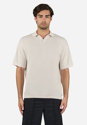 Beige short-sleeve polo shirt with a V-neck, textured ribbed pattern, and contrasting collar. Finishing detail includes a small logo label at the hem.